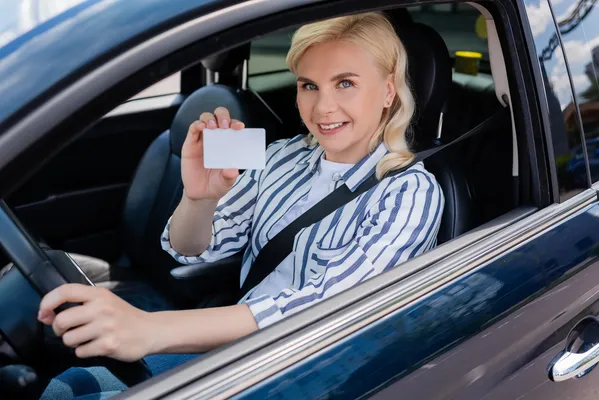 Mujer en un automóvil sonriendo enseñando una licencia de conducir que obtuvo gracias a los cursos de manejo VERTIZ